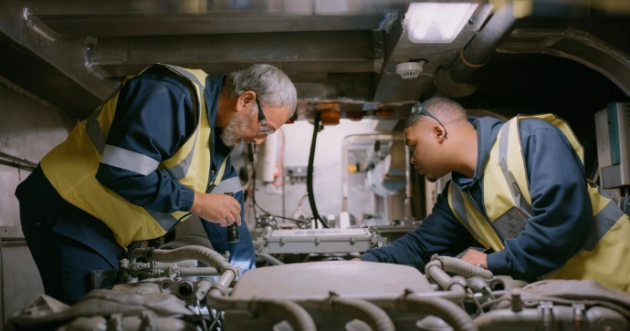 Two technicians inspecting fuel lines inside engine bay in yacht